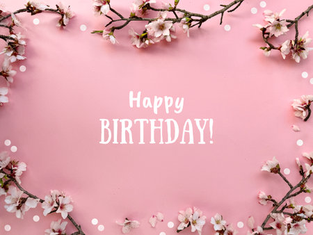 Text Happy Birthday in a frame with blossoming spring almond flowers on a pink paper backgroundの写真素材