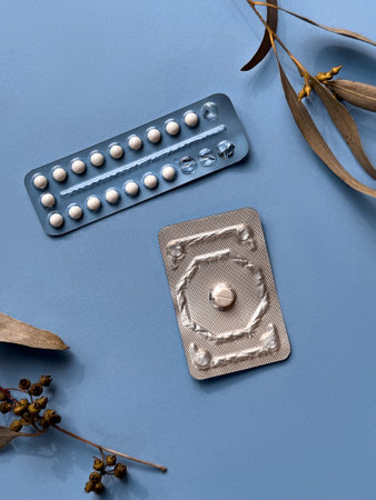 Two different packs of contraceptive pills on colored paper background with eucalyptus leaves, overhead view. Monthly pack and a morning-after pill.の写真素材