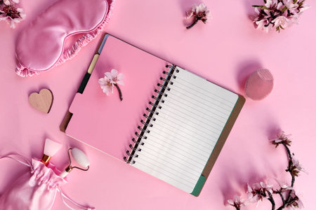 Square pink overhead background, quality of sleep, and self care routine. Sleeping mask, blank notebook with copy-space, massage stone roller.の写真素材