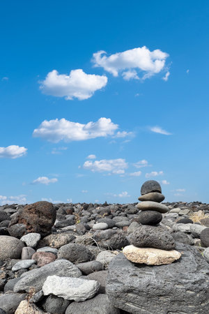 Zen-like stone pyramid on a wild volcanic shore with blue sky, clouds. Meditation, spiritual journeyの写真素材