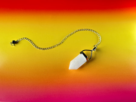White crystal pendant, pendulum on a chain, healing amulet, spiritual energy detector on vibrant orange and red paper backgroundの写真素材