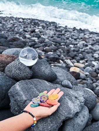Healing crystal and hand holding rainbow gemstones, chakra stones, on grey volcanic ocean shoreの写真素材