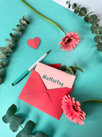 A red envelope with a note Muttertag, or Mothers day in German language, attached to it, lying on a mint green surfaceの写真素材
