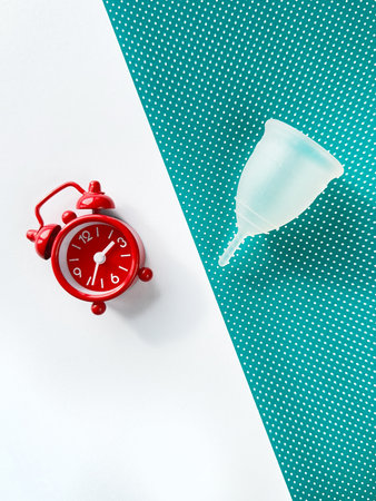 A reusable silicone menstrual cup and alarm clock on a green and white paperの写真素材