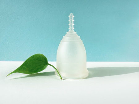 Reusable Menstrual Cup With Green Leaf on Blue Colored Paperの写真素材
