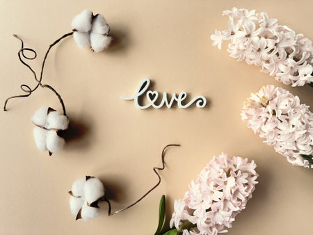 Spring composition with wooden word love, pink hyacinth and white cotton flowers on paper backgroundの写真素材