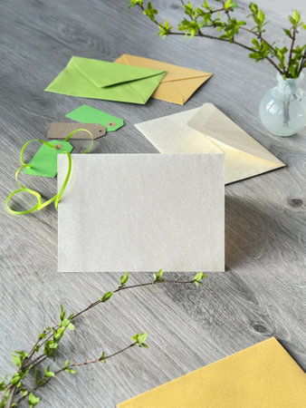 Minimalistic Stationery Display with Blank Card, Envelopes, Green Ribbon, and Spring Branchesの写真素材