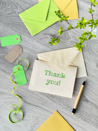 Spring-Themed Thank You Card with Green and Yellow Envelopes on a Wooden Deskの写真素材