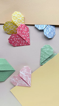 Colorful Origami Hearts in Varying Patterns Arranged Near Envelopes on Pastel Background