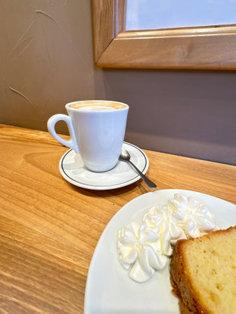 Coffee Cup with Cake Slice and Whipped Cream on Wooden Table in Cozy Cafe Settingの写真素材
