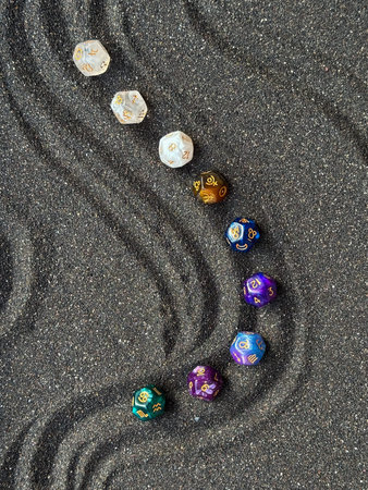 Colorful Polyhedral Dice Arranged on Black Sand with Curved Patterns for Game Enthusiasts