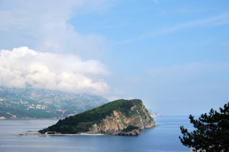 Scenic landscape of Sveti Nikola Island surrounded by the Adriatic Sea near Budva, Montenegro. Lush greenery covers the island, with mountains and clouds in the background.の写真素材