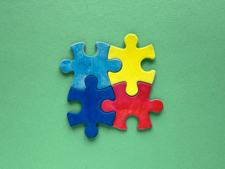 Autism World Awareness Day, four colorful puzzle pieces in blue, yellow, red, and green arranged together on a solid green surface, symbolizing teamwork and unity.の写真素材