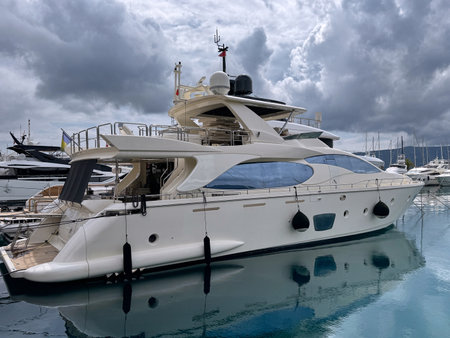 Elegant white luxury yacht moored in the serene waters of Port Montenegro marina. Overcast sky and reflections on the water create a tranquil atmosphere.の写真素材