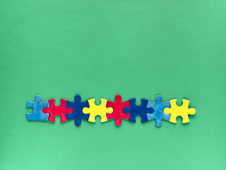 Row of colorful puzzle pieces in red, blue, and yellow on a plain green background. Autism World Awareness Day,の写真素材