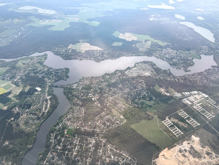 Aerial perspective of Berlin suburbs showcasing a winding river, dense forests, residential neighborhoods, and agricultural fields under a clear sky.の写真素材