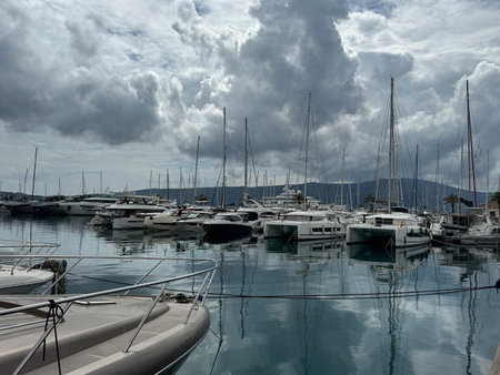 Luxury yachts and sailboats docked at the serene Porto Montenegro marina, reflecting on calm waters under dramatic cloudy skies. Mountains visible in the background.の写真素材