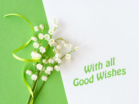 Lily of the valley flowers tied with a green ribbon placed on a white and green background. Text "With all Good Wishes" in green adds a cheerful message.の写真素材