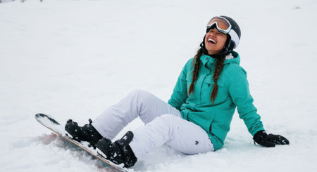 Woman sits on a snowy slope with her snowboard, laughing and relaxed during a winter sports outing while wearing a teal jacket and goggles, with a wide white background and available space for text or graphicsの素材
