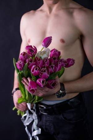 A young guy with a beautiful, naked torso holds in his hands a large bouquet of purple tulipsの写真素材