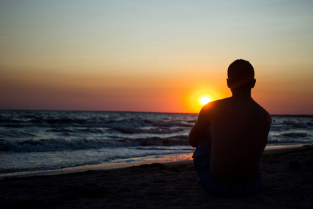 Silhouette of a young man with glasses looking at the sunset in the oceanの写真素材