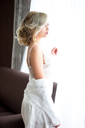 Beautiful girl with a hairdo in an air negligee.Pretty young girl. Blonde woman with luxurious long curly hair. Boudoir morning of the bride.の写真素材