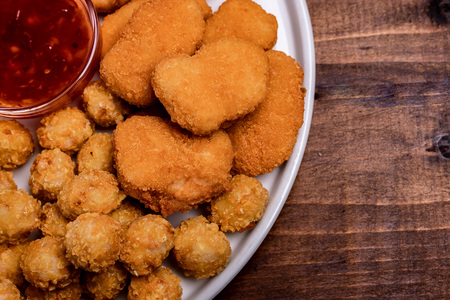 Snacks for beer on a white plate are: chicken nuggets, onion rings in tempura, chicken popcorn and chili sauceの写真素材