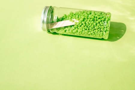 A JAR OF GREEN WAX GRANULES LIES ON A GREEN BACKGROUND.の写真素材