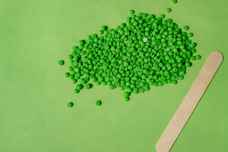 GREEN WAX GRANULES LIE ON A GREEN BACKGROUND, A ROW WITH A WOODEN SPATULA. SPACE FOR TEXT.の写真素材