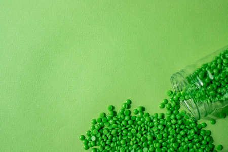 GRANULES OF GREEN WAX LIE ON A GREEN BACKGROUND, POURED FROM A TRANSPARENT JAR. SPACE FOR TEXT.の写真素材
