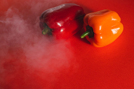 SWEET RED AND ORANGE PEPPERS ON A RED BACKGROUND WITH A LIGHT SMOKE