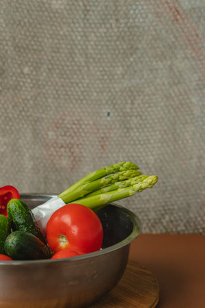 Vegetables lie in a metal bowl: tomatoes, asparagus, cucumbers, red bell peppers . on a wooden board...
