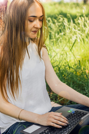 On the banner, a young girl works with a laptop in the fresh air in the park, sitting on the lawn....
