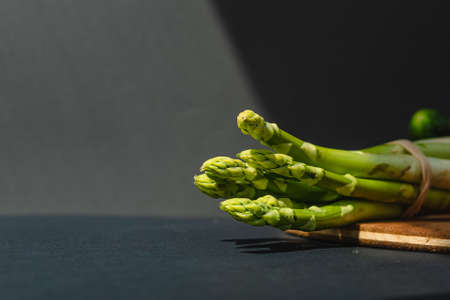 branches of fresh green asparagus on a wooden board, dark gray background, top view. Basic trend concept with copy spaceの写真素材