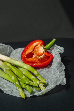 fresh green asparagus and half of red sweet, large pepper lie on white parchment on a dark gray background. proper nutrition. lifestyle. place for textの写真素材