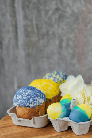 Easter cakes in the colors of the flag of Ukraine, yellow and blue in a cardboard stand with eggs, Easter eggs. place for text. selective focusの写真素材