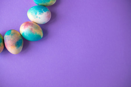 Easter composition with colorful eggs in shopping cart, wooden bunny and spring flowers on purple background. Easter frame of eggs painted in purple color. copy spaceの写真素材