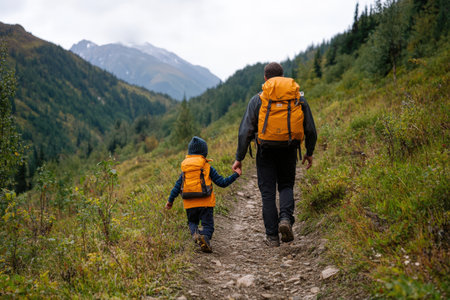 Father and son hiking in mountainous landscape with orange backpacks.の素材