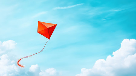 Bright orange kite soaring in clear blue sky with fluffy white clouds.の写真素材