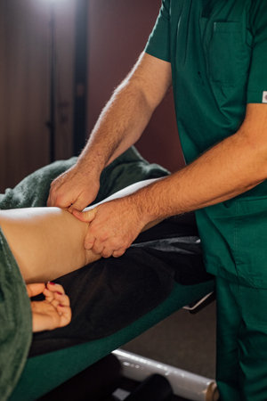 Male adult performing therapeutic leg massage on relaxed client in spa setting.の写真素材
