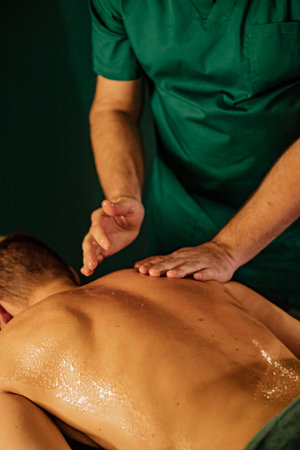 Male body massage therapy session with practitioner in green attire.