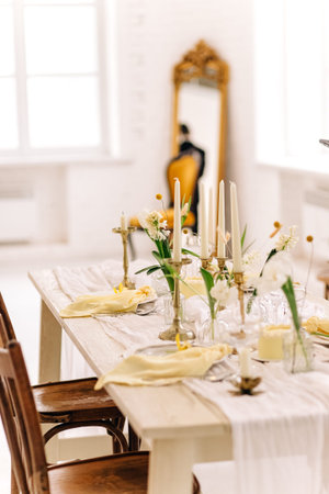 Elegant dining table setup with candles and yellow accents in bright interior.