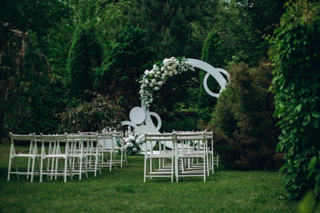 Outdoor wedding ceremony setup with white chairs and floral arch in lush garden.の写真素材
