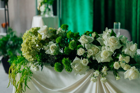 Elegant white and green floral arrangement on table with green backdrop.の写真素材