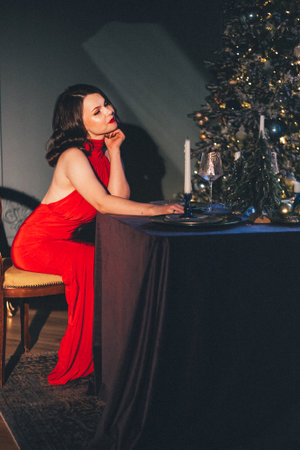 Caucasian young female in elegant red dress at candlelit dinner near Christmas tree.の写真素材
