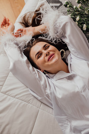 Relaxed young caucasian female in white shirt with flowers laying on bed smiling.の写真素材