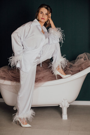 Caucasian young female in stylish feathered pajamas posing confidently in bathtub.の写真素材