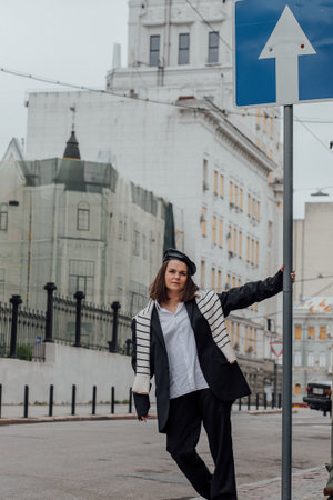 Confident young caucasian female standing near urban traffic sign in stylish outfit.の写真素材
