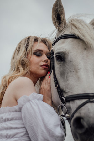 Young caucasian female bonding with white horse outdoors.の写真素材