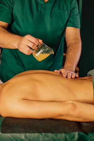 Male massage therapist applies oil on young adult patient for relaxation therapy.の写真素材